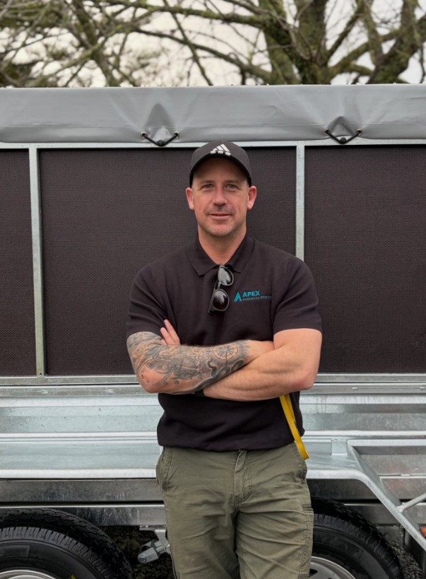 Apex Asbestos Removal team member in branded uniform in front of an Apex work trailer